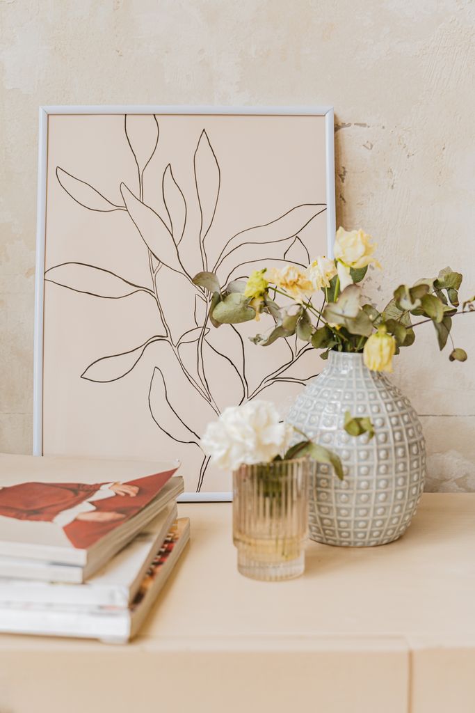 A stylish display of a line art frame with vases and flowers on a wooden shelf for home decor inspiration.